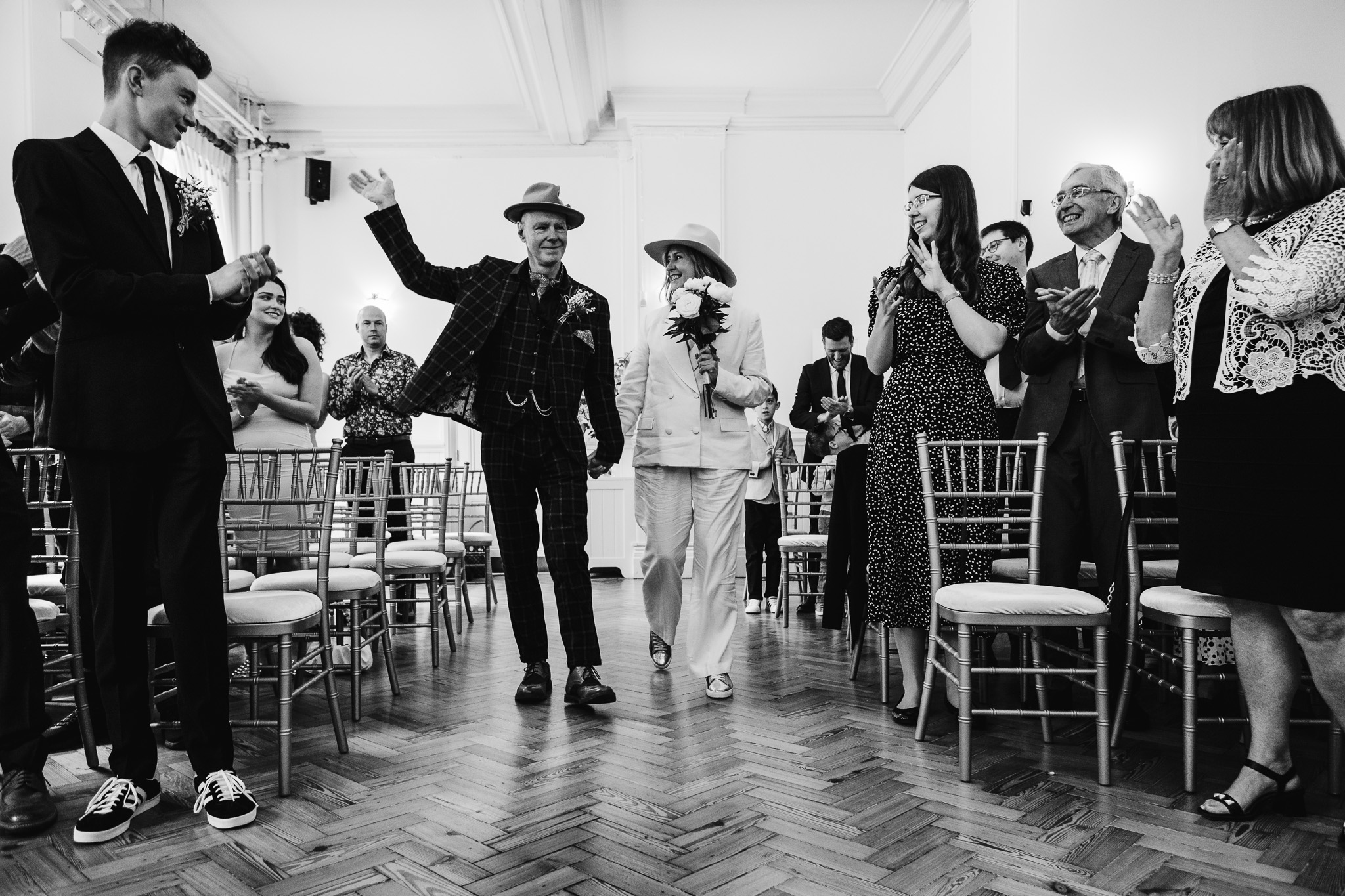 Mary and Mike walk down the aisle together whilst their guests clap on either side of them at Brighton Town Hall.