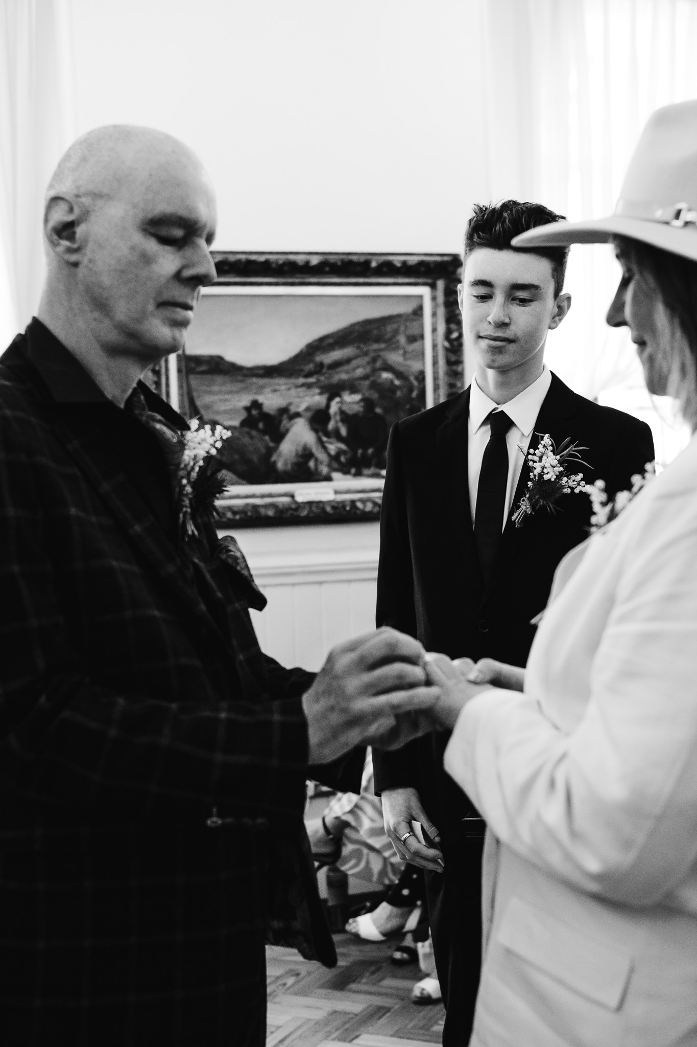 The bride and groom's son watches over them as they exchange wedding rings during their wedding ceremony.