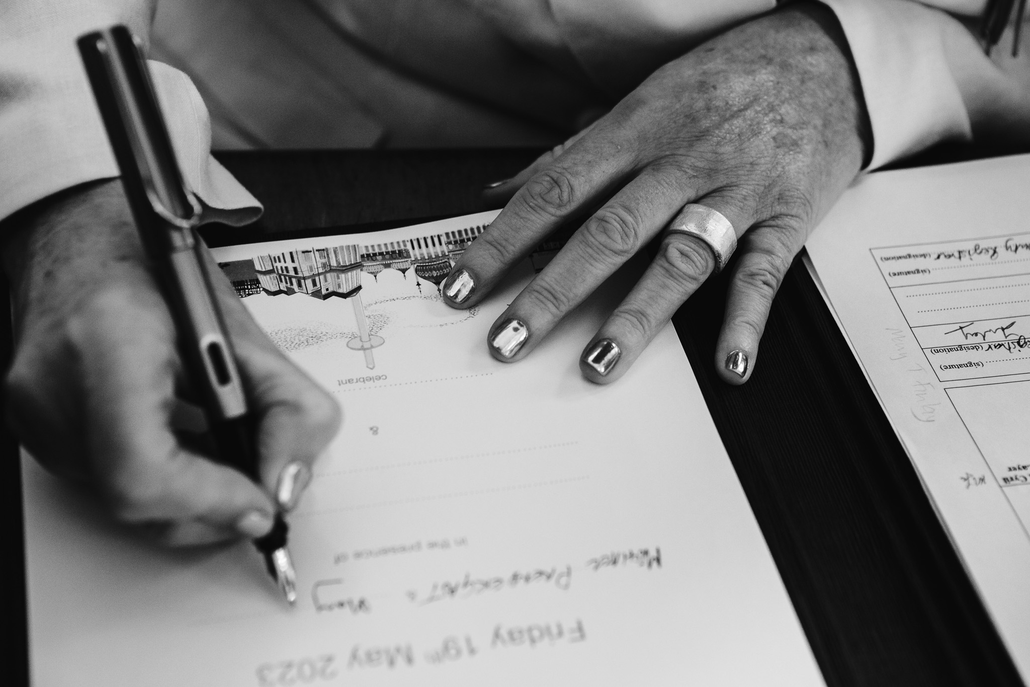The bride's hands signing her wedding certificate with a beautiful silver manicure.
