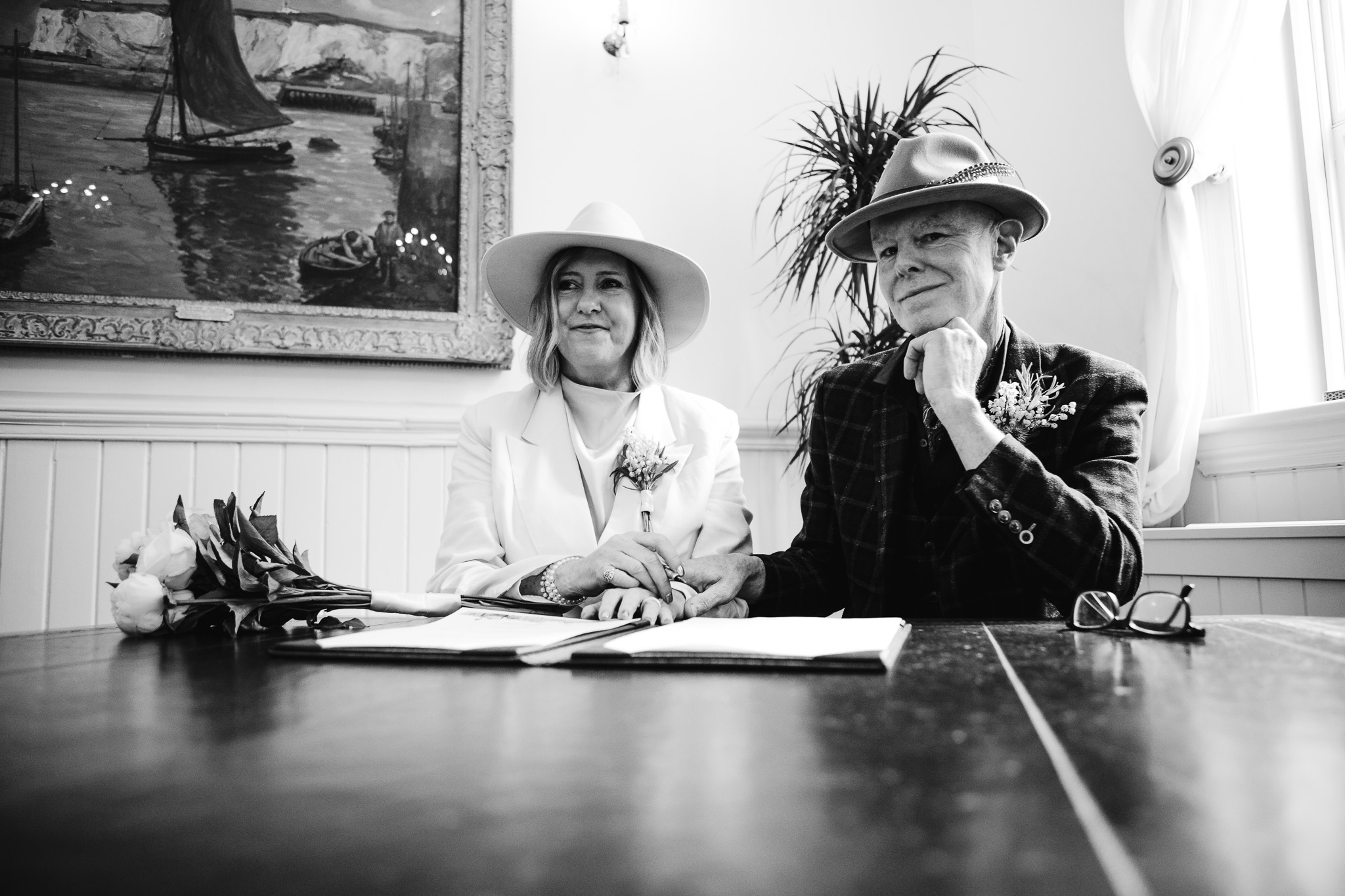 Mary and Mike sit and pose at a desk after signing their marriage certificates at Brighton Town Hall.
