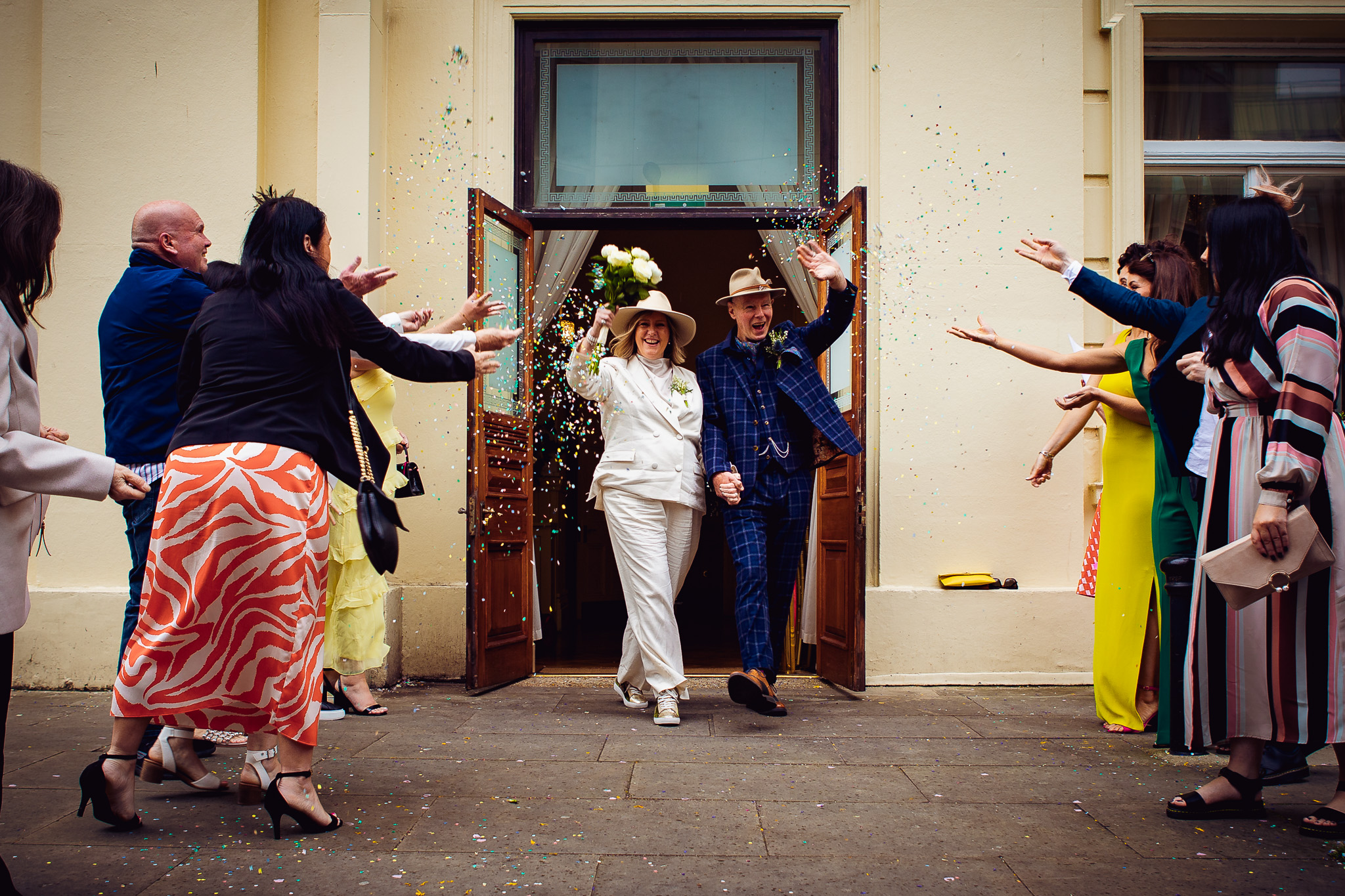 Mary and Mike walk through smiling at their guests as they throw confetti after their wedding ceremony at Brighton Town Hall.