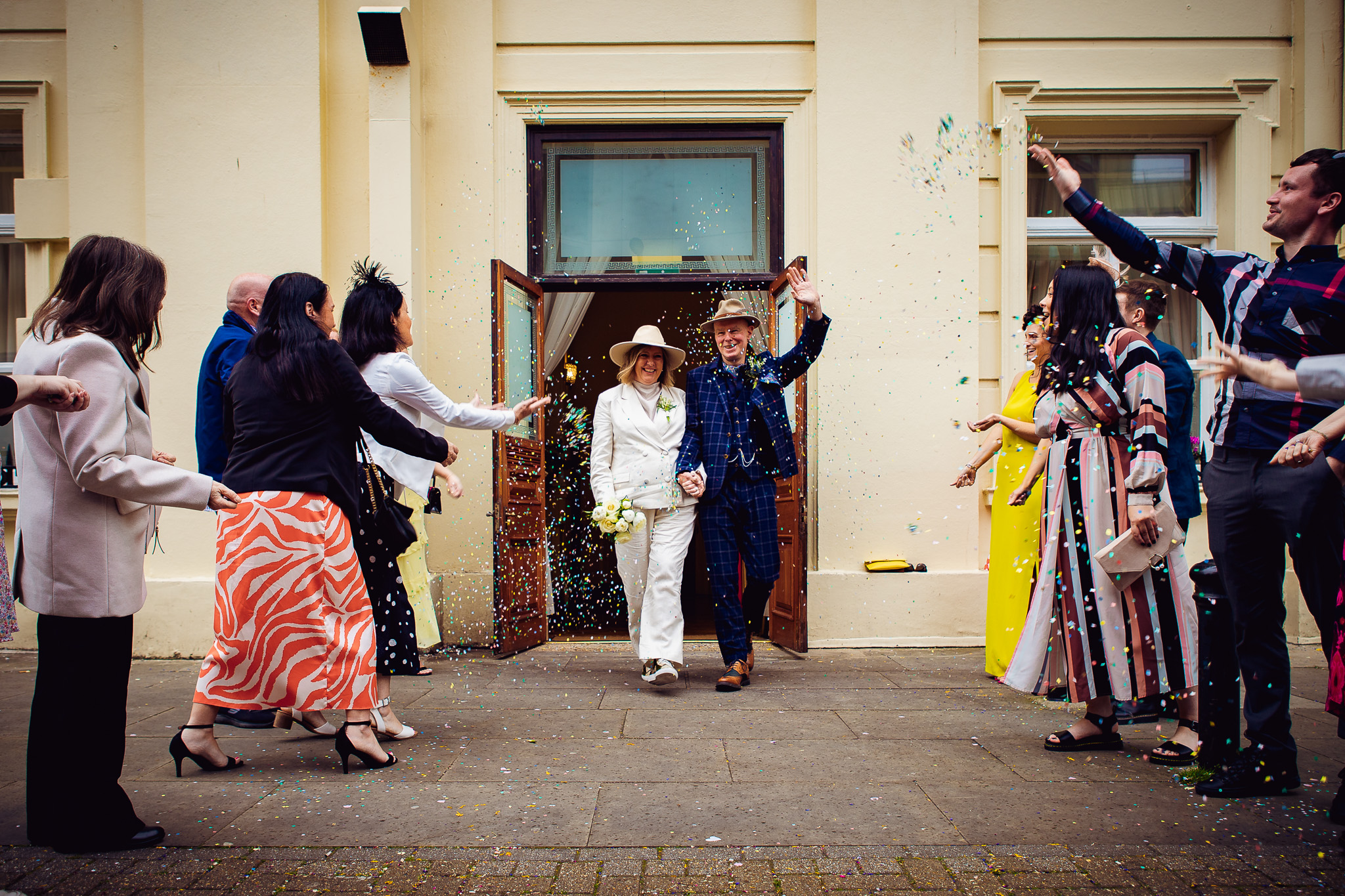 Mary and Mike walk out of Brighton Town Hall after their wedding ceremony through their guests as they throw confetti.