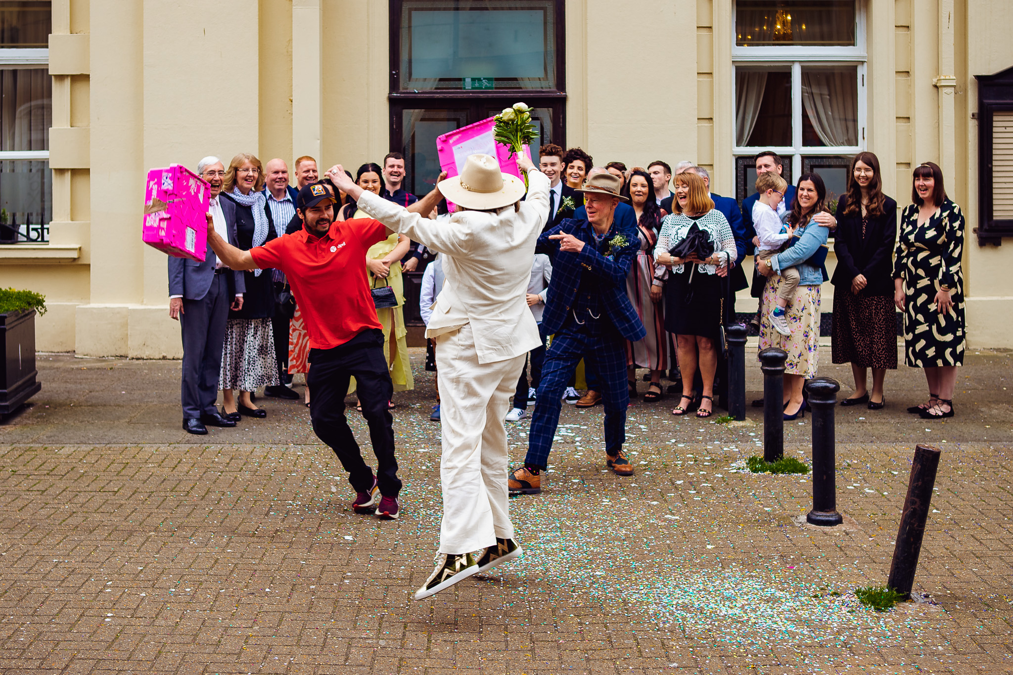 Bride jumps up as a postal worker photobombs a group shot outside of Brighton Town Hall.