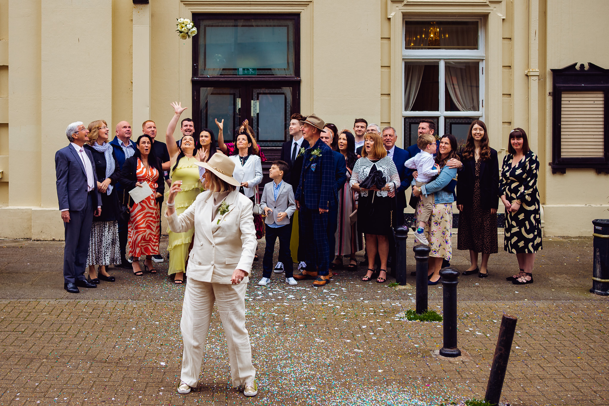Wedding guests reach to catch the brides bouquet that has been thrown outside of Brighton Town Hall.