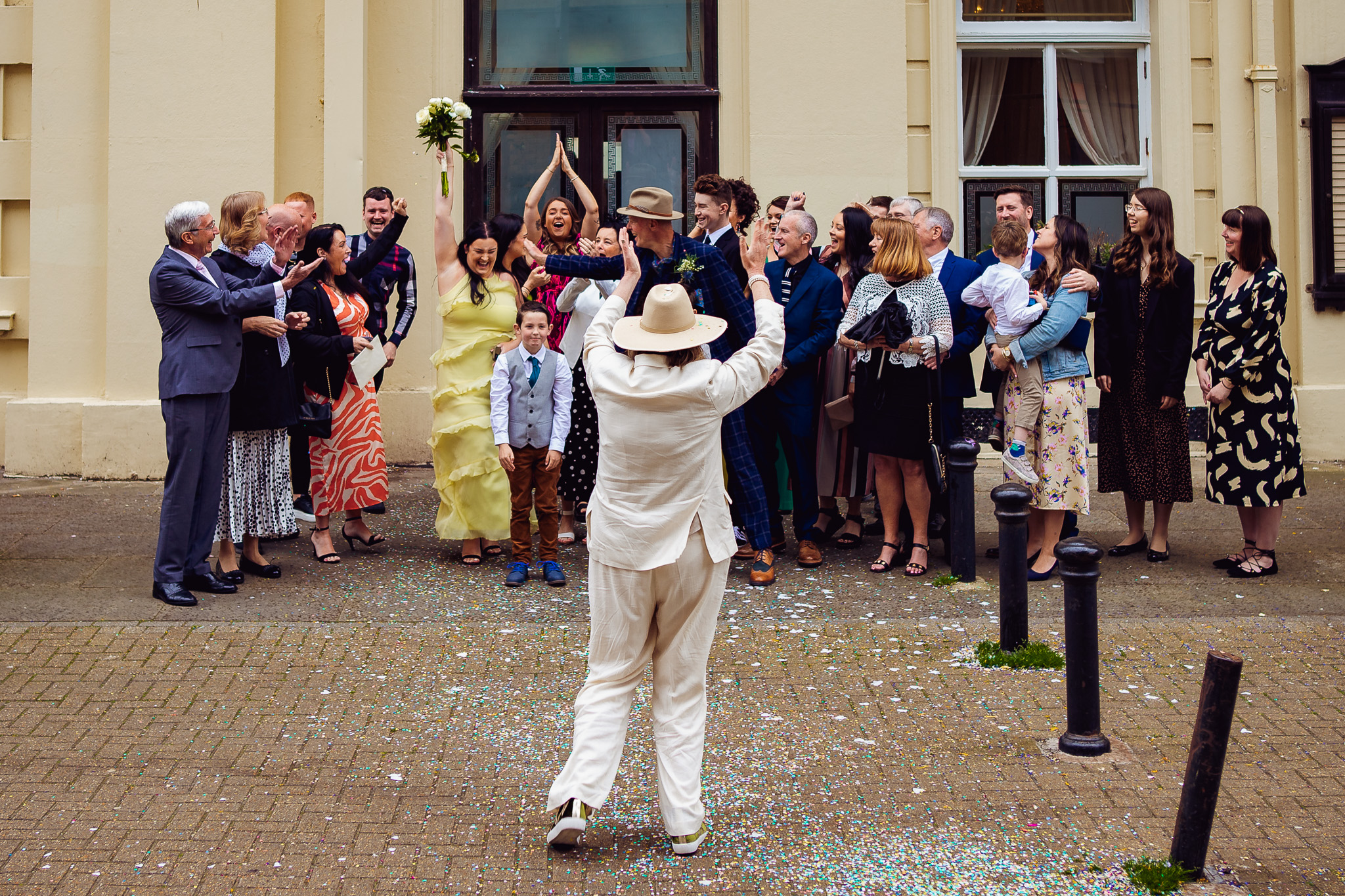 Woman in yellow dress has caught the wedding bouquet as guests cheer outside of Brighton town Hall.
