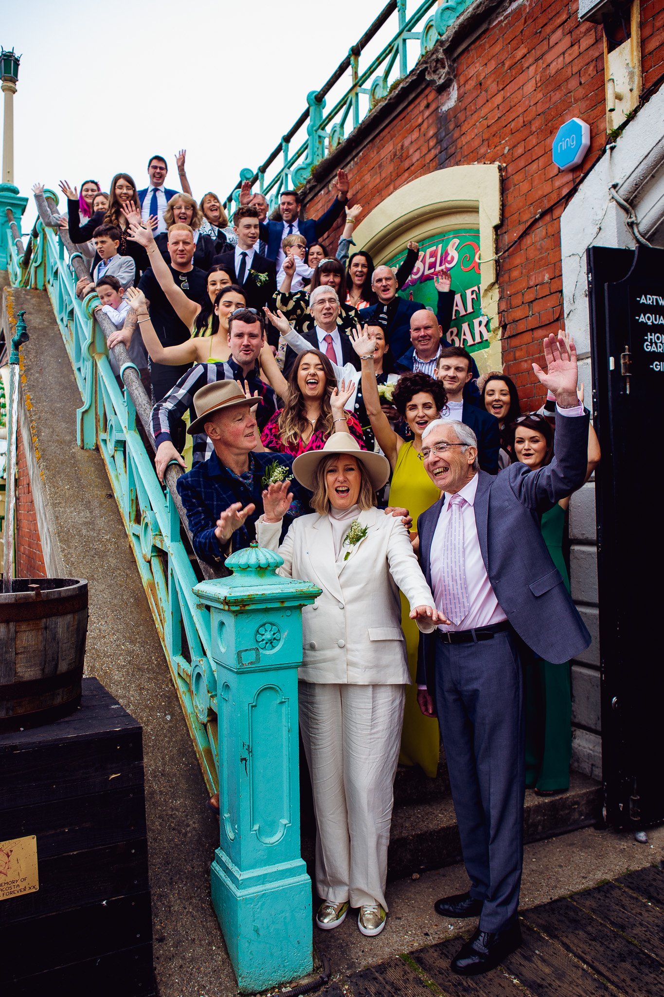 Mary, Mike and all their wedding guests pose for the wedding group shot on the stairs down to Brighton beach.
