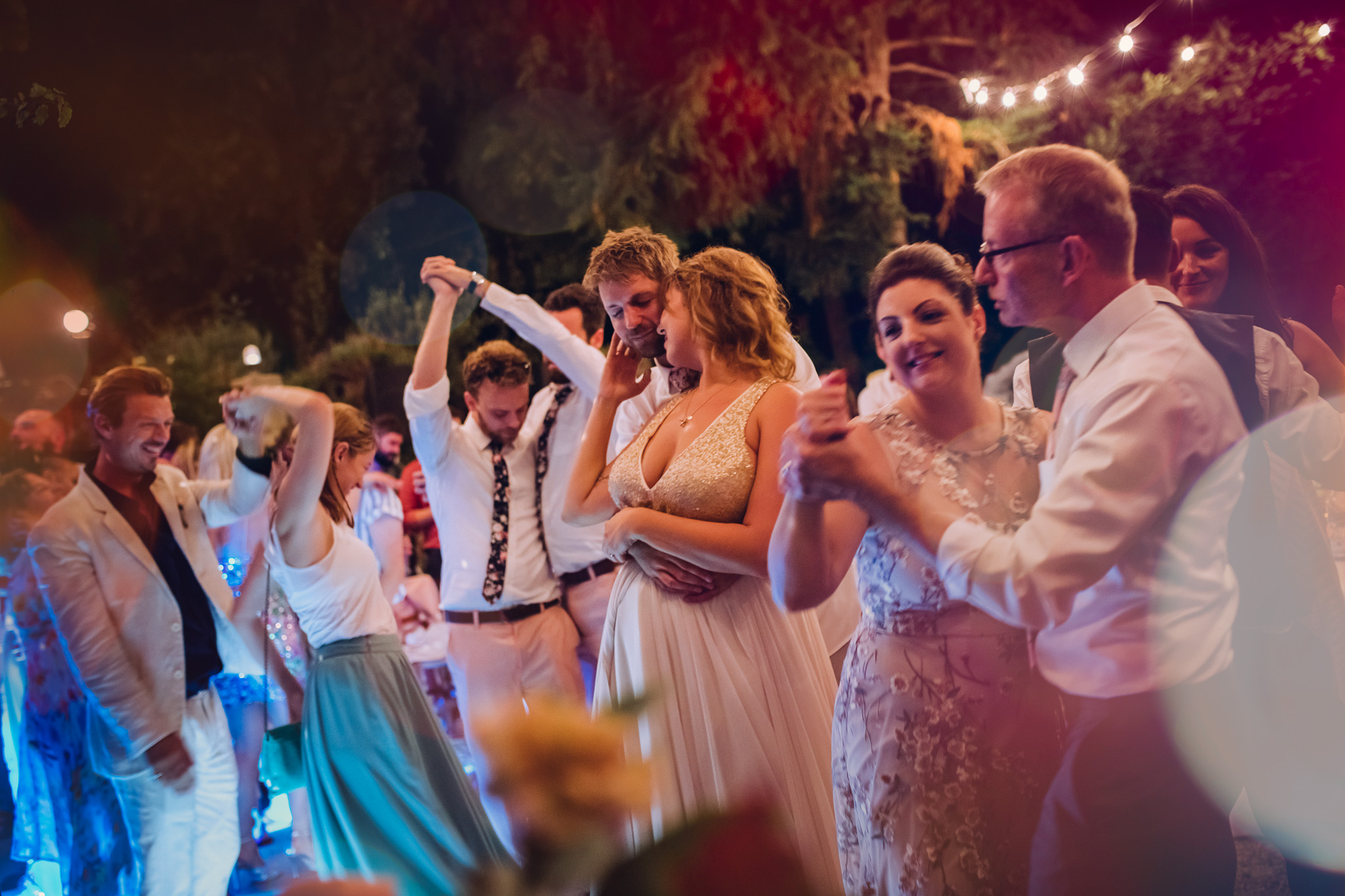 Olga and Mark embrace and share a private moment whilst the guests dance at a wedding reception in Crete