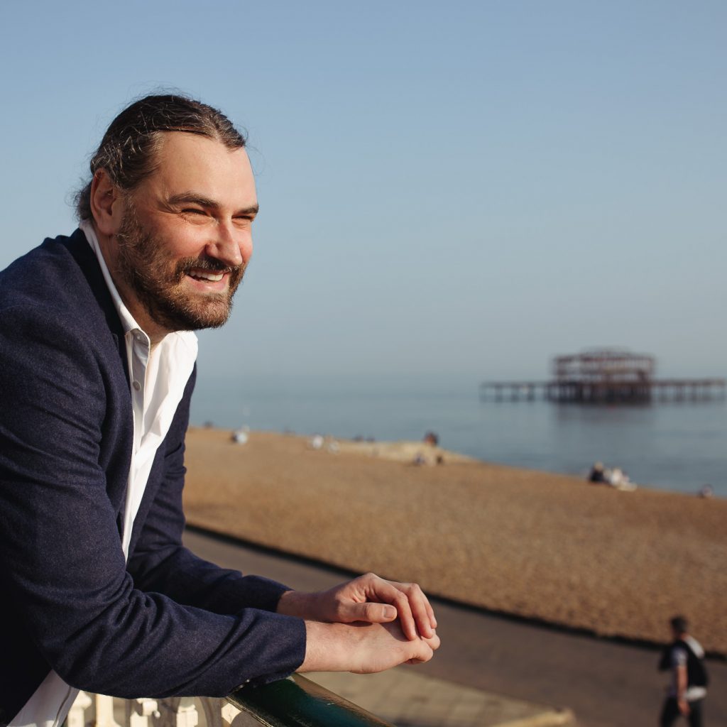 outdoor headshot of a smiling young professional man at Brighton West Pier