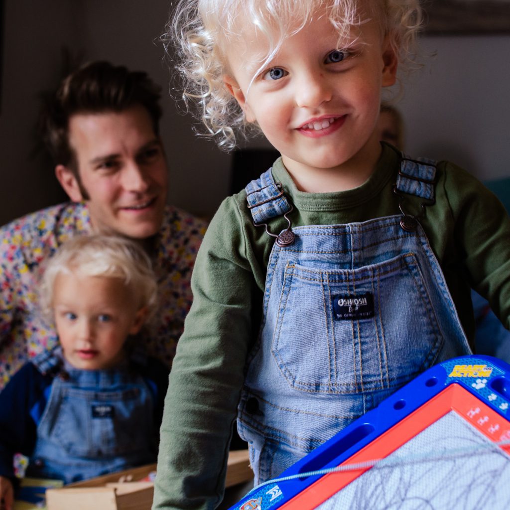 A young boy with is dad and twin brother showing an etch a sketch during a family photo session